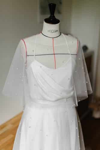 zoom auf die Vorderseite einer drapierten Brauttop und eine Cape mit perlen. Elegant und moderne Flair