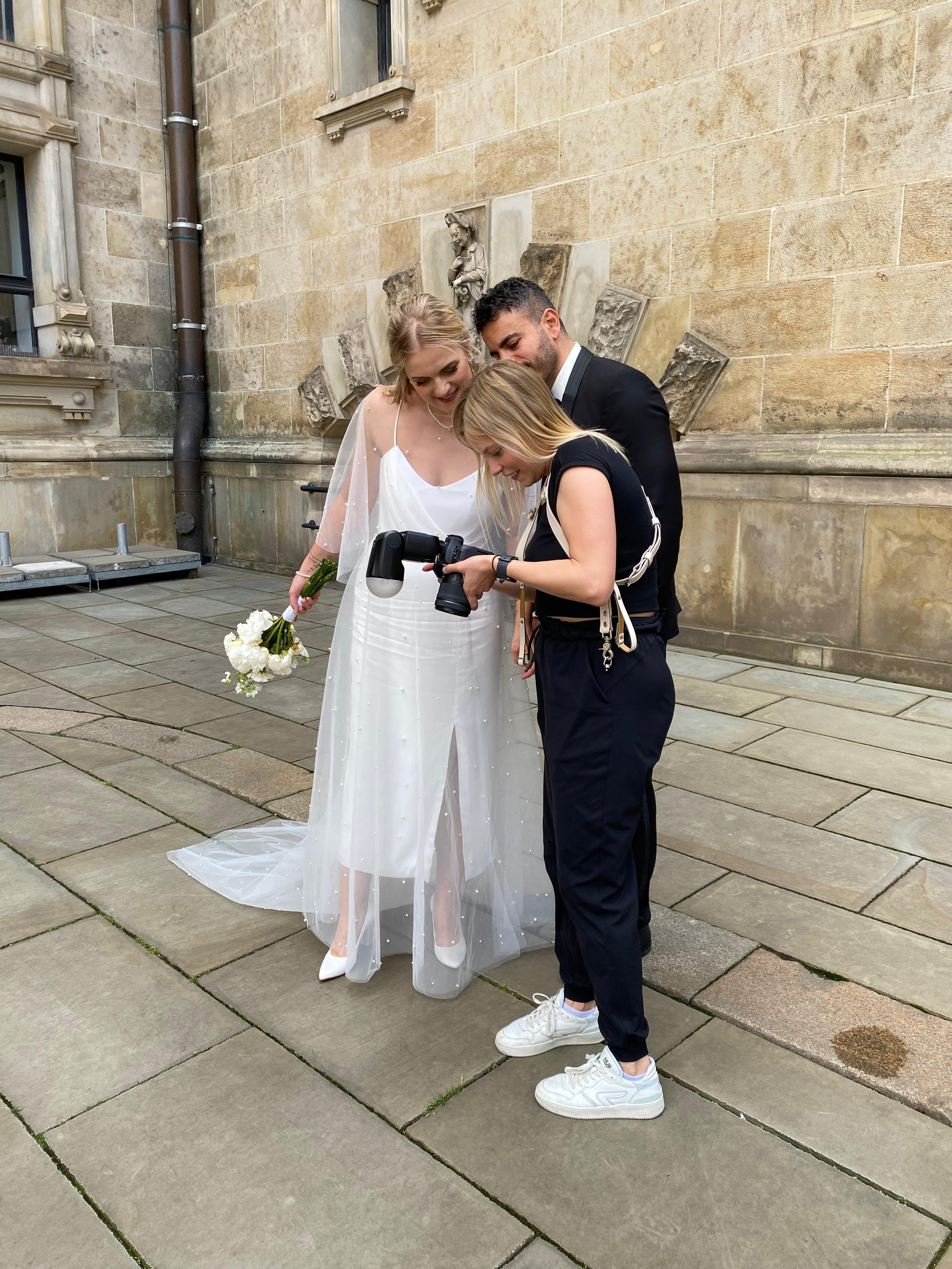 Fotografin zeigt einem Hochzeitspaar Fotos. Die Braut trägt ein tragbares Brautkleid, bestehend aus einem elegant brautRock und einem urban brauttop