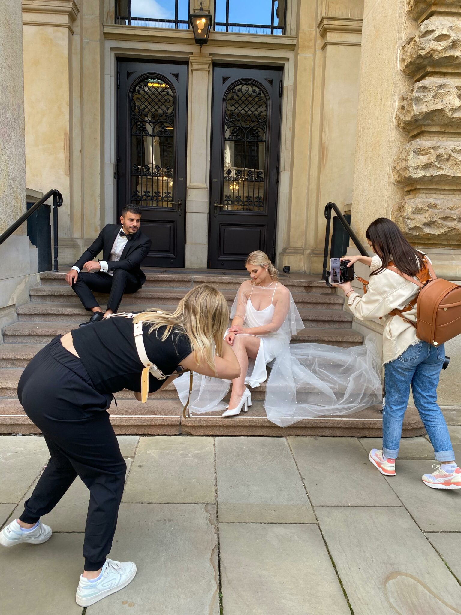 Fotografinnen fotografieren ein Brautpaar vor dem Hamburger Rathaus. Das Brautkleid besteht aus einen Hochzeitsrock und ein Hochzeitsoberteil sowie eine abnehmbare Schleppe aus perlenbesetztem Tüll. urban und elegant Look